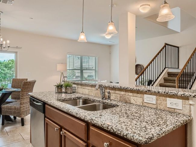 Kitchen with a sink, stainless steel dishwasher, light stone counters, hanging light fixtures, and light tile patterned floors | Image 4