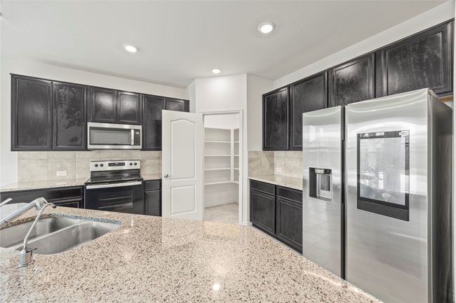 Kitchen with stainless steel appliances, dark cabinets, a sink, tasteful backsplash, and light stone counters | Image 8