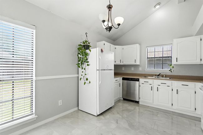 Kitchen featuring stainless steel dishwasher, freestanding refrigerator, light marble finish flooring, white cabinetry, and lofted ceiling | Image 11