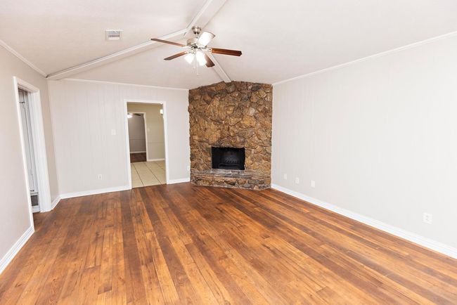 Unfurnished living room with ceiling fan, a fireplace, wood-type flooring, crown molding, and baseboards | Image 5