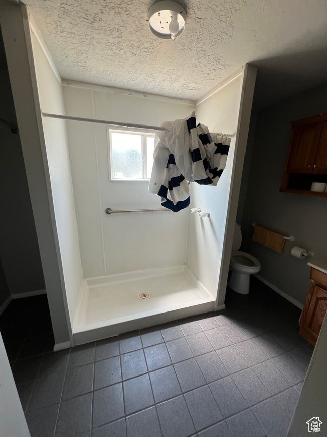 Full bathroom with a textured ceiling, a shower stall, toilet, and tile patterned flooring | Image 8