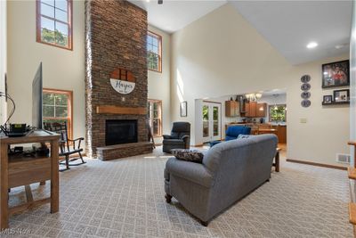 Carpeted living room with a high ceiling, a healthy amount of sunlight, a chandelier, and a fireplace | Image 3