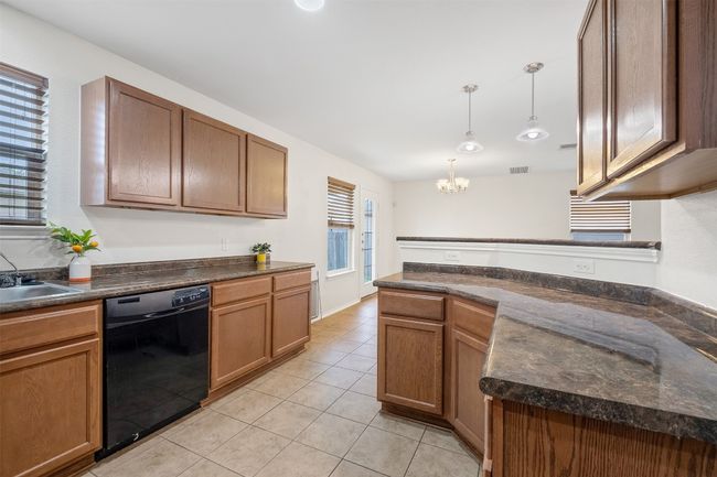 Kitchen with light tile patterned flooring, dark countertops, a chandelier, black dishwasher, and decorative light fixtures | Image 8