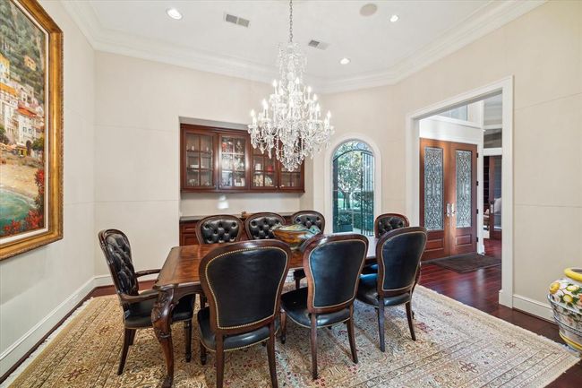 This elegant dining room features a classic wooden table with leather chairs, a stunning chandelier, and a built-in glass cabinet. Large windows provide natural light, while a decorative rug and artwork add warmth and sophistication. | Image 8