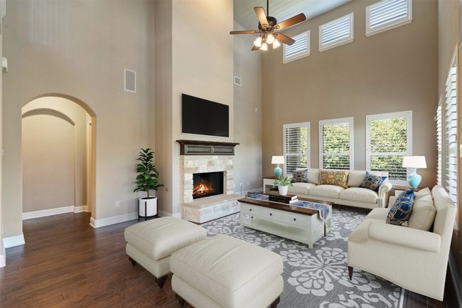 Living room featuring a high ceiling, wood finished floors, arched walkways, ceiling fan, and a stone fireplace | Image 14