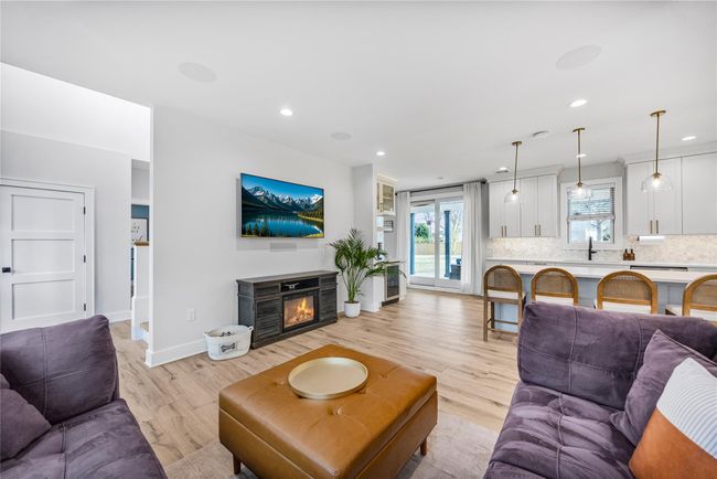 Living room with light wood finished floors, baseboards, recessed lighting, beverage cooler, and a glass covered fireplace | Image 8