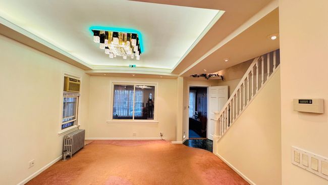 Carpeted entrance foyer featuring radiator, a tray ceiling, stairs, a chandelier, and a wall mounted air conditioner | Image 4