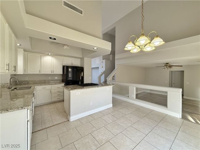 Kitchen with visible vents, black appliances, ceiling fan with notable chandelier, a sink, and a raised ceiling | Image 12