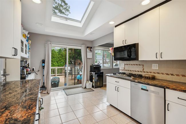 Kitchen featuring stainless steel appliances, a skylight, decorative backsplash, beverage cooler, and recessed lighting | Image 7