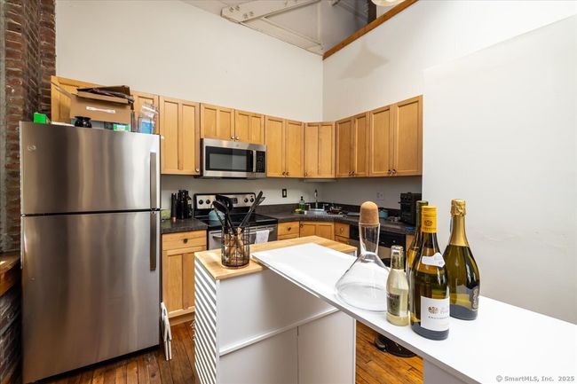 Modern-industrial kitchen with exposed brick walls, high ceilings, and large windows allowing ample natural light, featuring wooden cabinetry and stainless steel appliances | Image 8