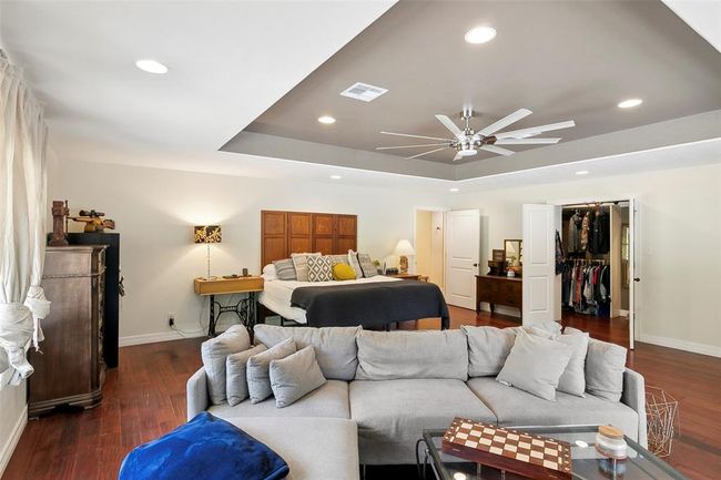This spacious master bedroom features a cozy sitting area with a sectional sofa, a large bed, and a walk-in closet. It has wood flooring, recessed lighting, and a modern ceiling fan, creating a comfortable and stylish retreat. | Image 26