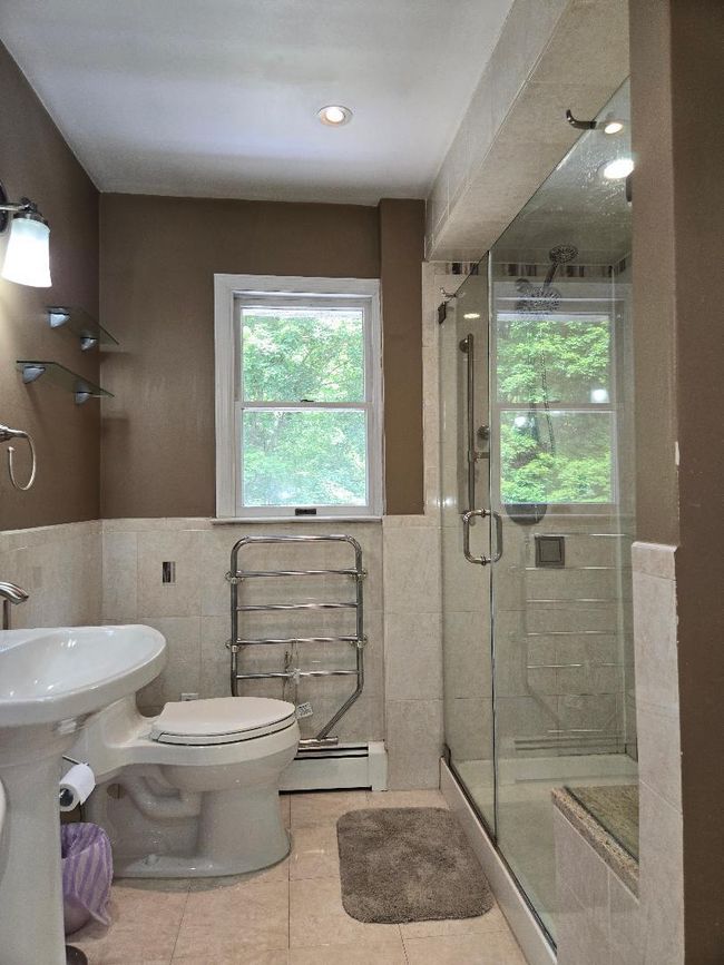 Bathroom with a baseboard heating unit, tile walls, tile patterned flooring, a stall shower, and a wainscoted wall | Image 19