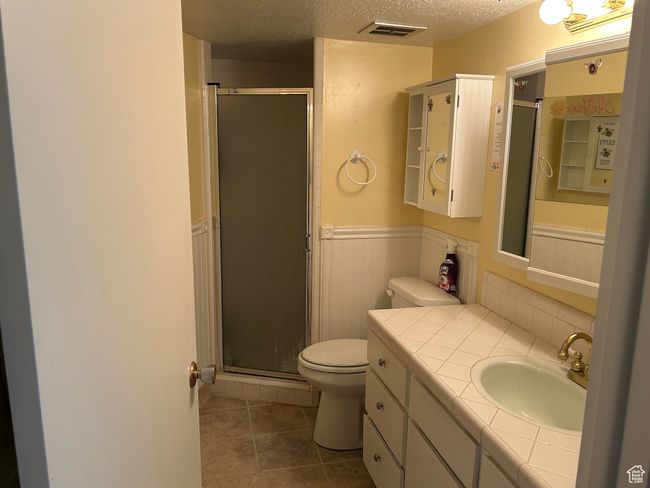 Full bathroom featuring toilet, a wainscoted wall, vanity, a stall shower, and a textured ceiling | Image 11