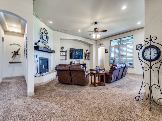 Carpeted living room featuring crown molding, arched walkways, a ceiling fan, a tile fireplace, and baseboards | Image 7
