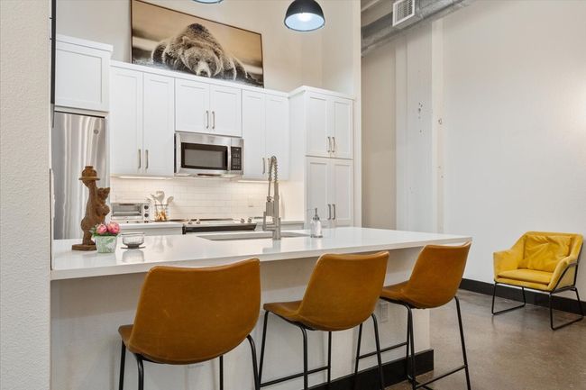 Kitchen featuring stainless steel microwave, decorative backsplash, a breakfast bar, and white cabinetry | Image 7