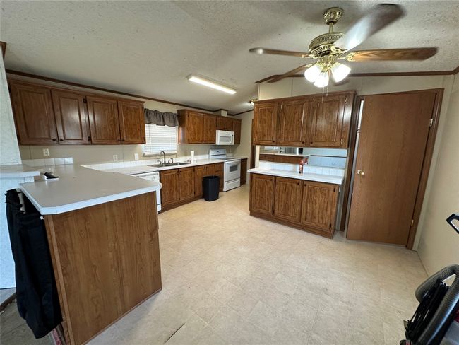 Kitchen featuring white appliances, a peninsula, lofted ceiling, ceiling fan, and a textured ceiling | Image 11
