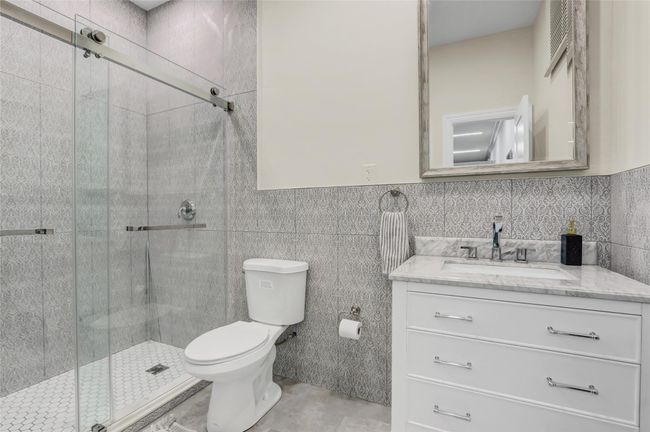 Bathroom with toilet, vanity, a stall shower, and tile walls | Image 30