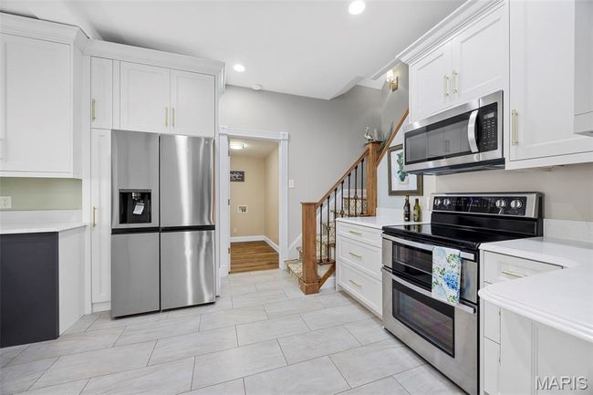 Kitchen with stainless steel appliances, light countertops, white cabinets, recessed lighting, and light tile patterned floors | Image 8