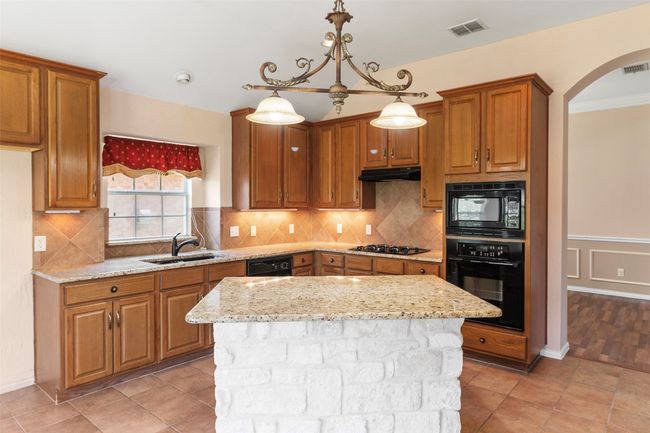 Kitchen with black appliances, a sink, arched walkways, under cabinet range hood, and brown cabinets | Image 28