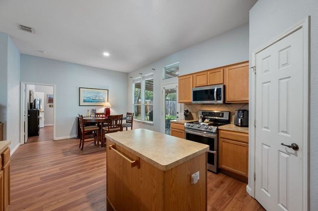Kitchen with appliances with stainless steel finishes, a kitchen island, wood finished floors, backsplash, and light countertops | Image 11
