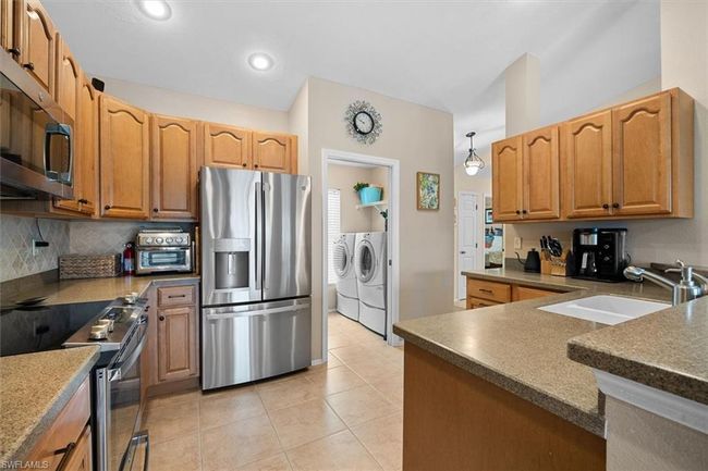 Kitchen featuring a sink, light tile patterned flooring, separate washer and dryer, backsplash, and appliances with stainless steel finishes | Image 13