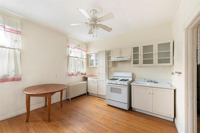 Kitchen featuring radiator heating unit, light wood-style flooring, white gas stove, under cabinet range hood, and a sink | Image 12