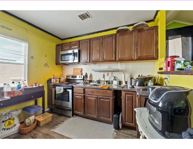Kitchen featuring plenty of natural light, stainless steel appliances, dark countertops, dark wood-style flooring, and crown molding | Image 35
