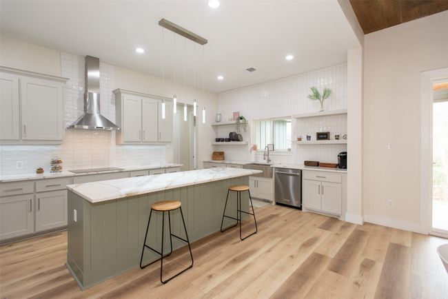 Kitchen with stainless steel dishwasher, a kitchen island, wall chimney exhaust hood, and a breakfast bar area | Image 7
