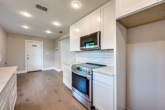 Kitchen featuring stainless steel appliances, decorative backsplash, light wood-style flooring, light stone countertops, and white cabinetry | Image 11
