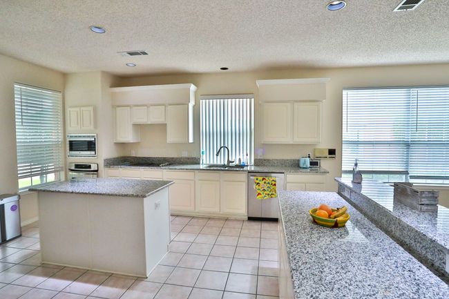 Kitchen featuring appliances with stainless steel finishes, a textured ceiling, light tile patterned flooring, light stone counters, and white cabinetry | Image 5