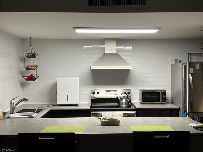 Kitchen featuring wall chimney exhaust hood, appliances with stainless steel finishes, tasteful backsplash, and light countertops | Image 7