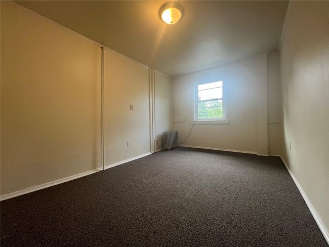 Empty room with radiator heating unit, dark carpet, and baseboards | Image 9