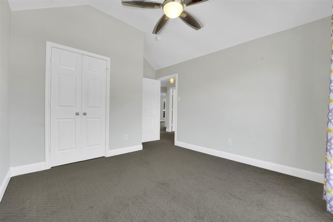 Unfurnished bedroom with lofted ceiling, dark colored carpet, a closet, and a ceiling fan | Image 20