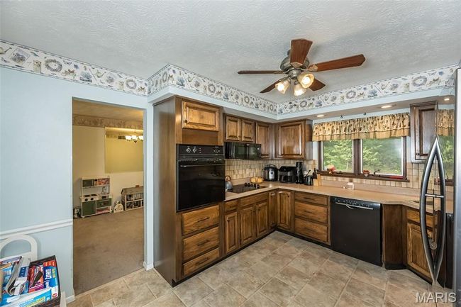 Kitchen with black appliances, ceiling fan, light countertops, a chandelier, and backsplash | Image 13