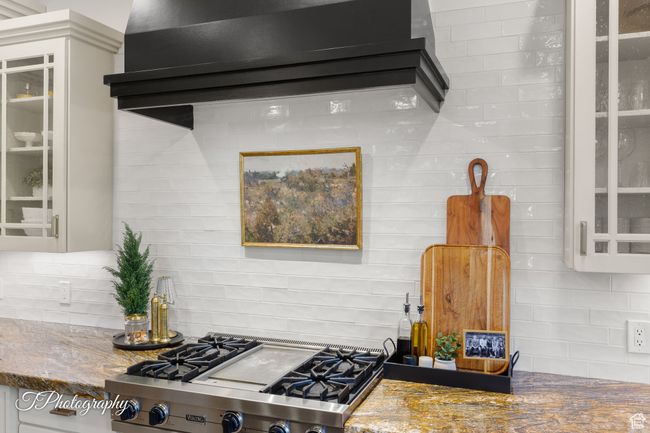 Kitchen featuring designer stove, tasteful backsplash, stone countertops, glass insert cabinets, and white cabinetry | Image 19