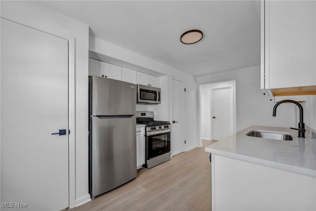 Kitchen with a sink, appliances with stainless steel finishes, white cabinetry, light wood-style flooring, and light stone counters | Image 12