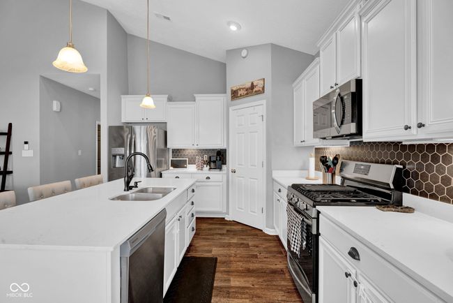 kitchen featuring stainless steel appliances, decorative light fixtures, a sink, backsplash, and light countertops | Image 13