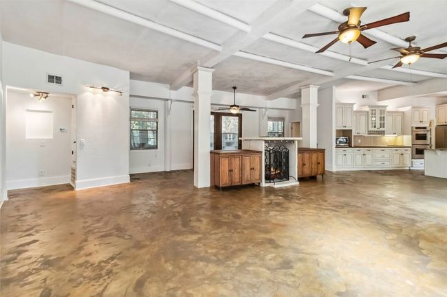 Living room, ceiling fan, concrete flooring, beamed ceiling, ornate columns, and a fireplace | Image 10