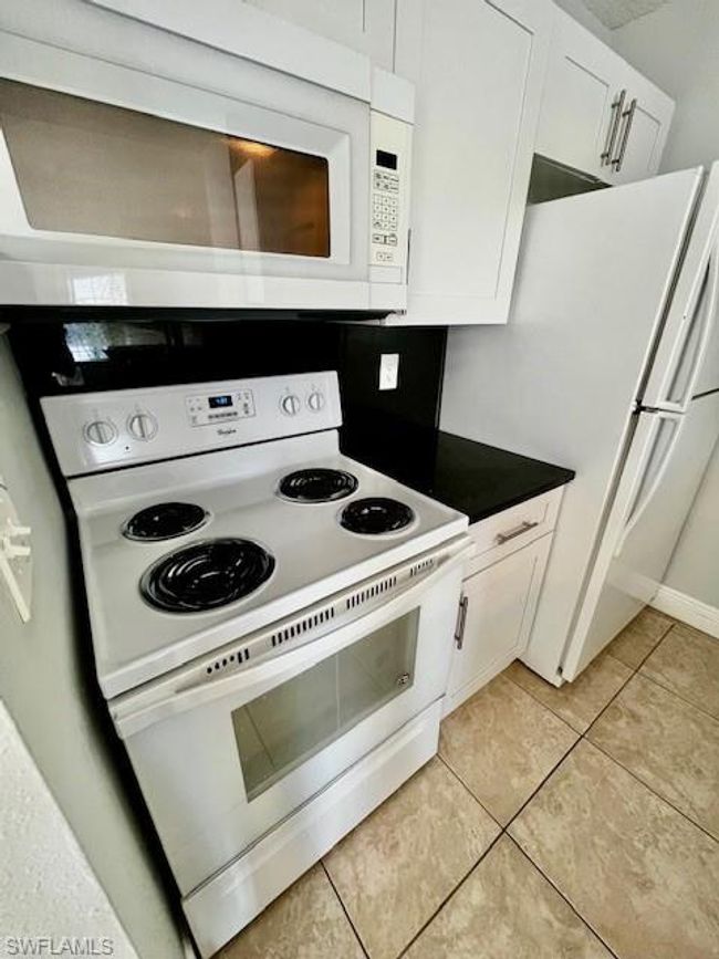 Kitchen with light tile patterned floors, dark countertops, white cabinetry, and white appliances | Image 13