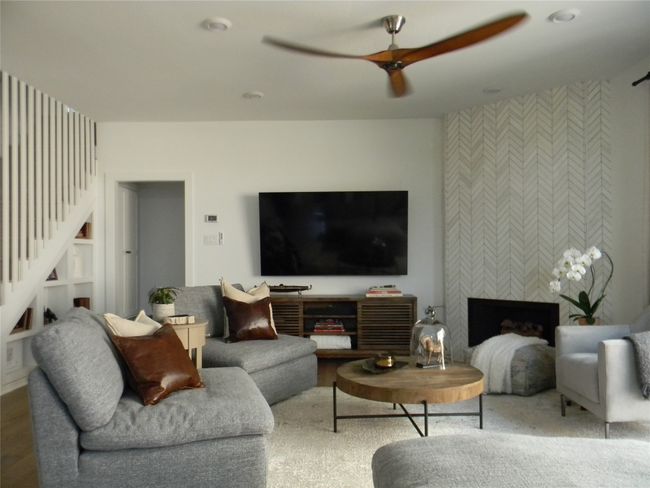 Living room featuring a ceiling fan, stairway, and marble tiled fireplace with adjacent slider doors to access side patio for entertaining | Image 5