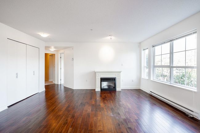 Unfurnished living room featuring wood-type flooring, baseboards, baseboard heating, and a glass covered fireplace | Image 8