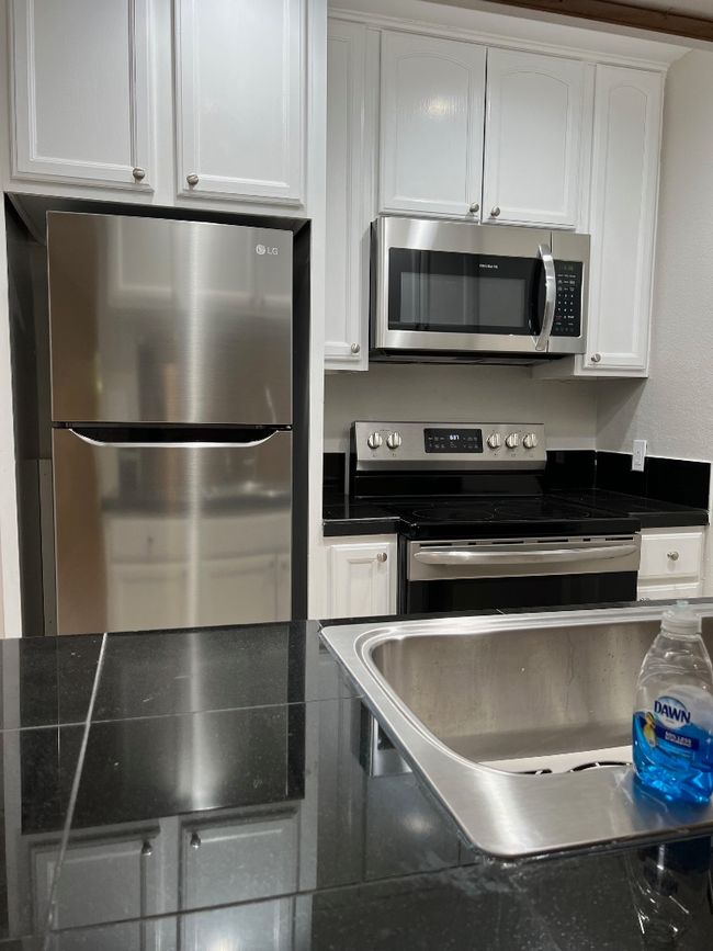 Kitchen with white cabinetry, dark countertops, fridge, and range with electric stovetop | Image 5