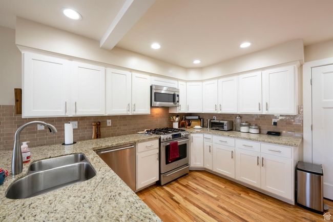 Kitchen with appliances with stainless steel finishes, a sink, backsplash, and white cabinets | Image 20