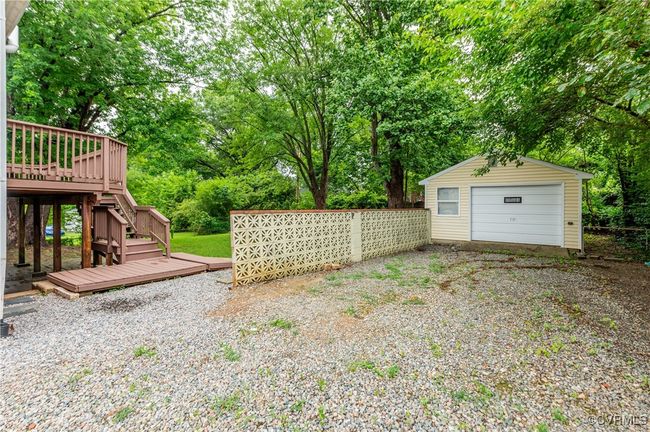 View of yard featuring a wooden deck, a detached garage, an outdoor structure, stairway, and view of scattered trees | Image 32