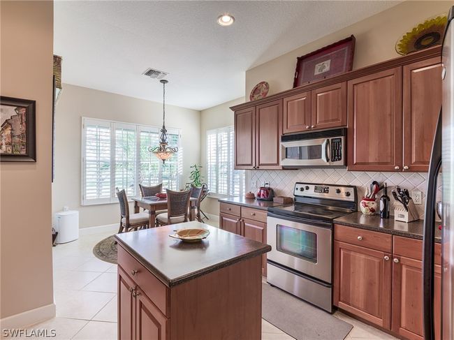 Kitchen featuring a center island, light tile floors, backsplash, and appliances with stainless steel finishes | Image 7