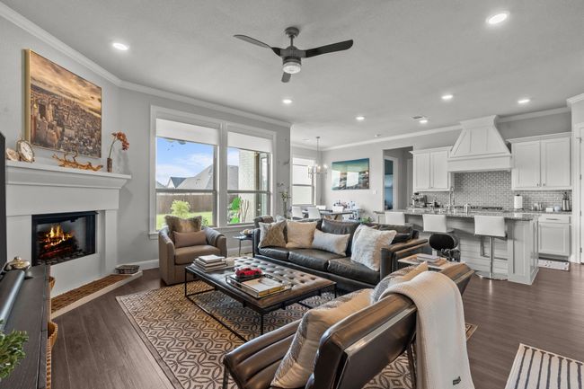 Living area featuring crown molding, a ceiling fan, a glass covered fireplace, recessed lighting, and dark wood-type flooring | Image 10