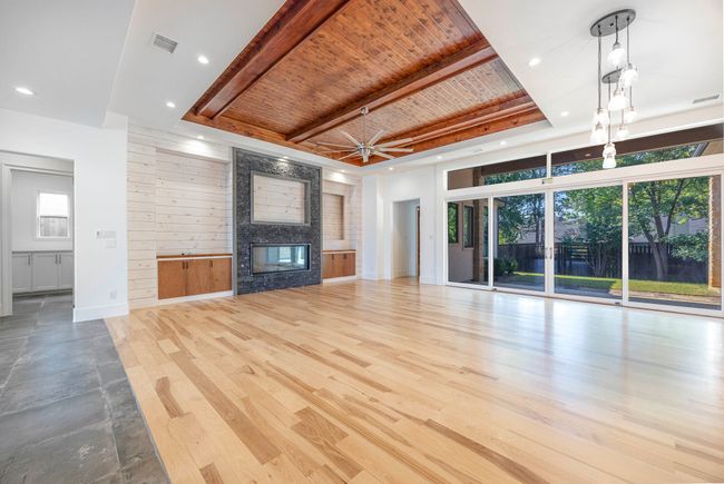 Unfurnished living room with a large fireplace, wood finished floors, wood walls, a raised ceiling, and a wood ceiling with exposed beams | Image 5