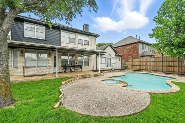 Rear view of house featuring brick siding, a patio area, a chimney, a fenced backyard, and a pool with connected hot tub | Image 32