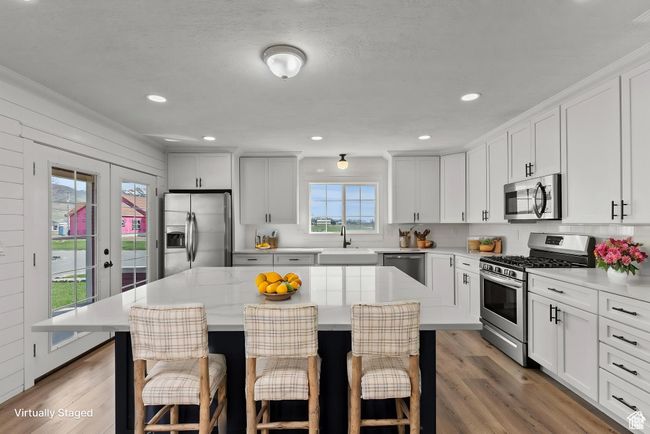 Kitchen with white cabinets, appliances with stainless steel finishes, a center island, light wood finished floors, and recessed lighting | Image 11