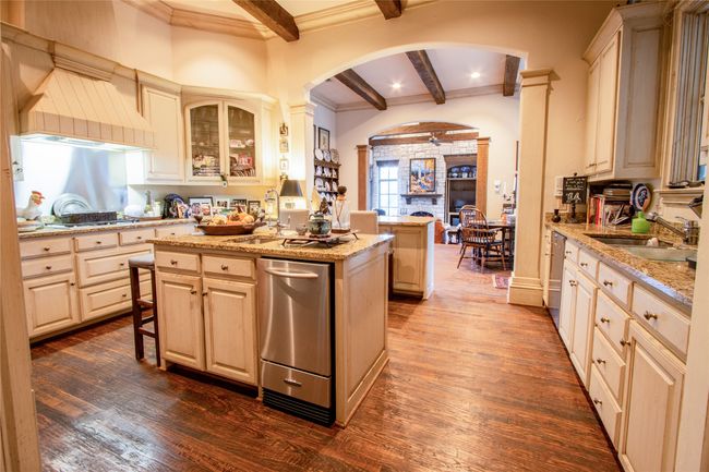 Kitchen with beam ceiling, a sink, dark wood finished floors, a center island, and arched walkways | Image 6